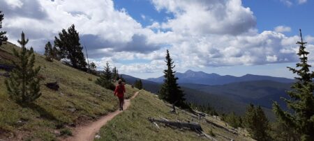 A single hiker on a mountain side trail, sunny day with clouds developing.