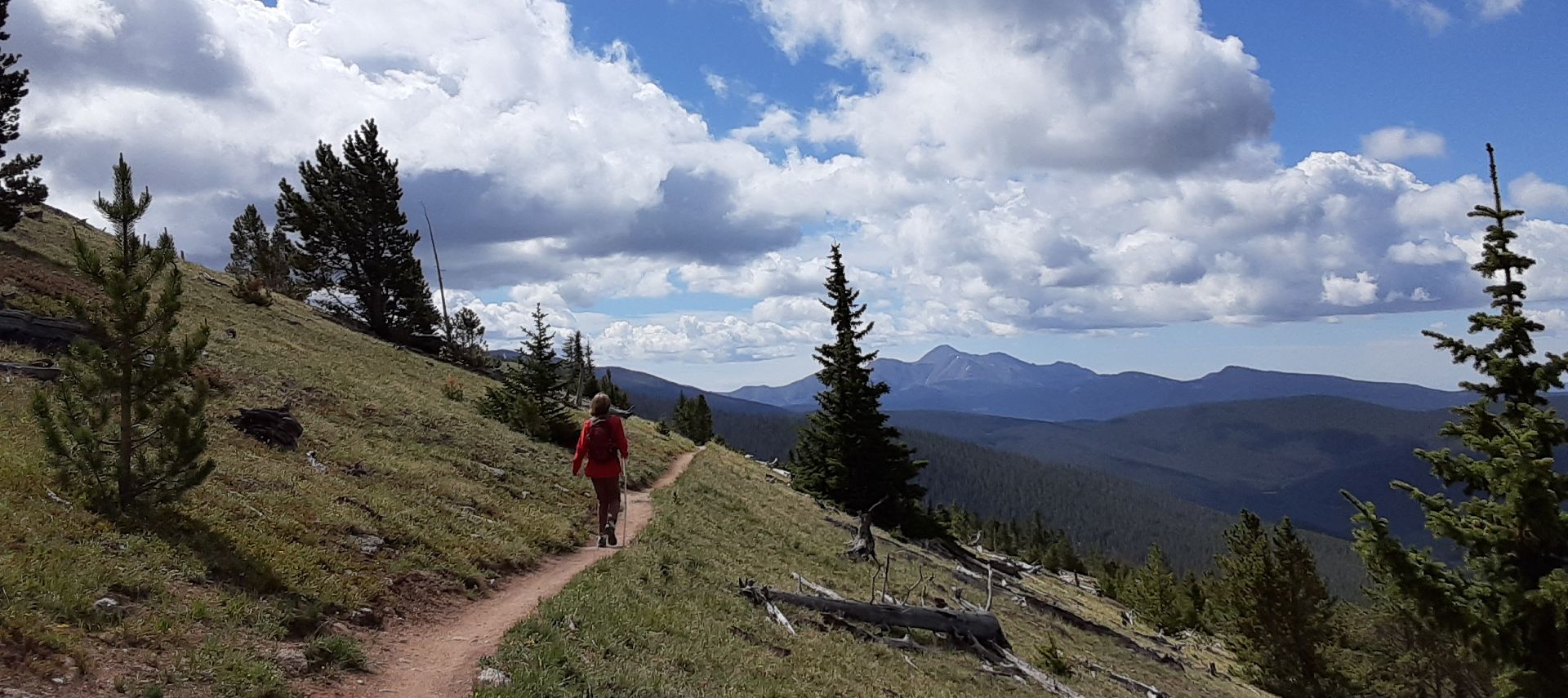 A single hiker on a mountain side trail, sunny day with clouds developing.