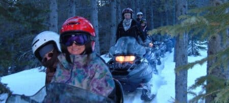 Four people snowmobiling in the woods.