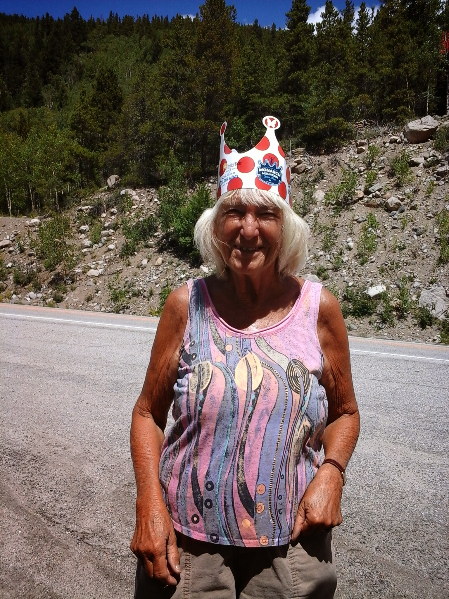 Lady standing on the side of a mountain pass with a paper crown on her head.