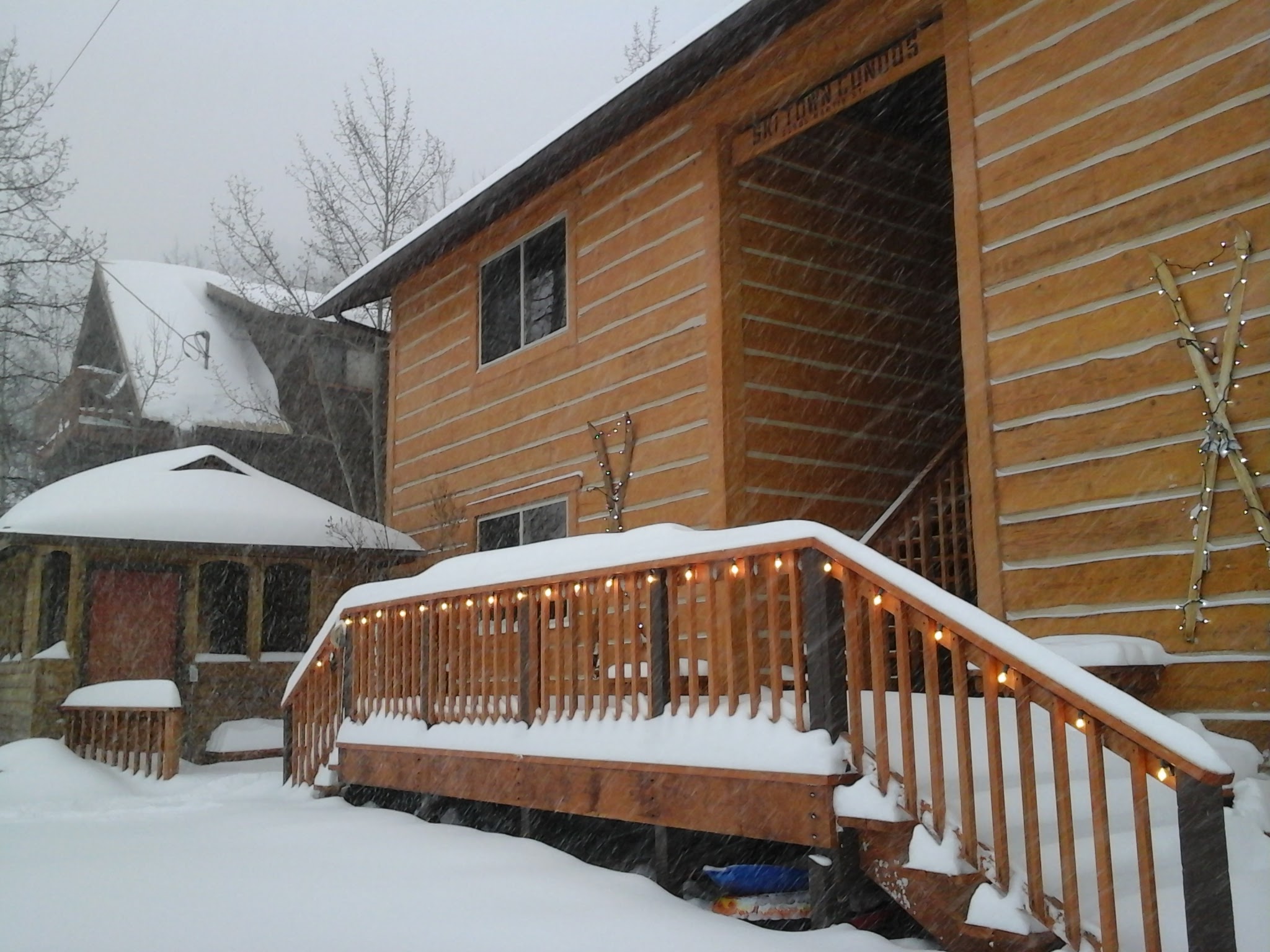 Exterior photo of condos with snow falling, six inches of snow and lights shining along the deck railing.