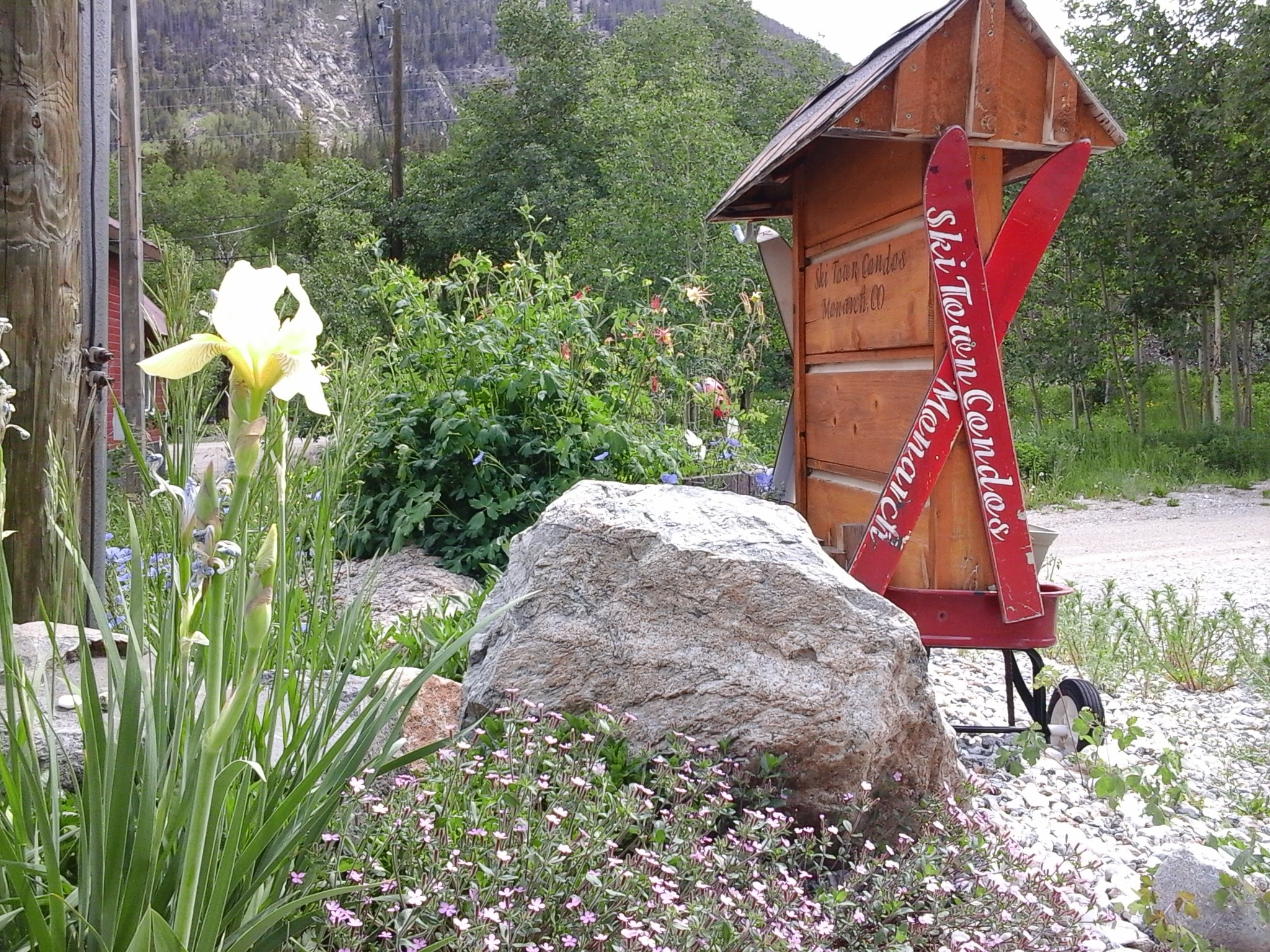 Exterior photo of flowers and wagon with crossed skis attached to Ski Town Condos sign.  Mountain in the background.