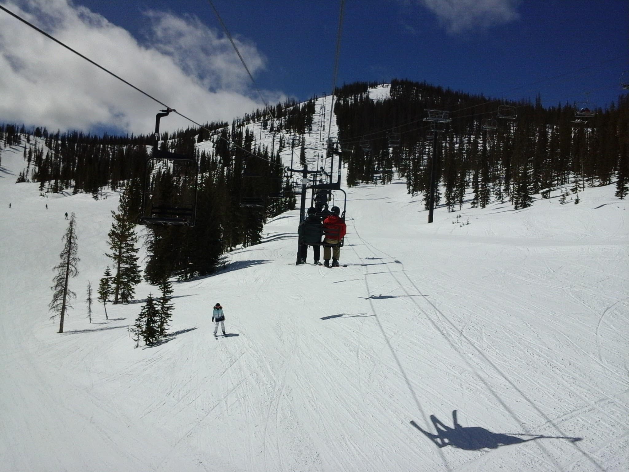 Exterior ski area with blue skys.  People riding on a chair lift.