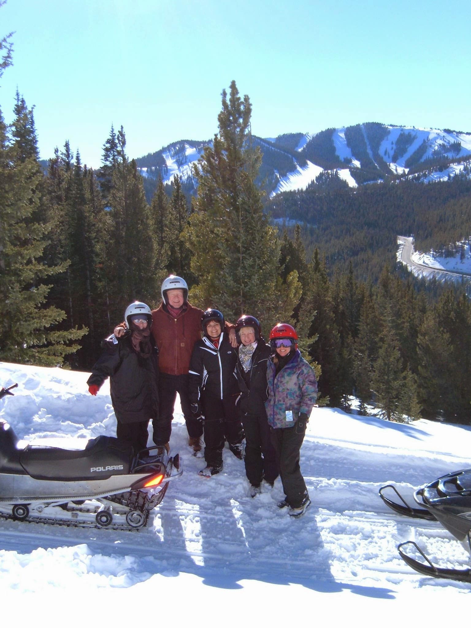 Five people taking a picture near their snowmobiles.