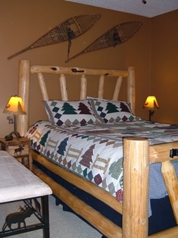 Bedroom with a log bed, down comforter, brown walls, snowshoes hanging on the wall, with beige carpet.  Moose theme bedside lamps and tables.