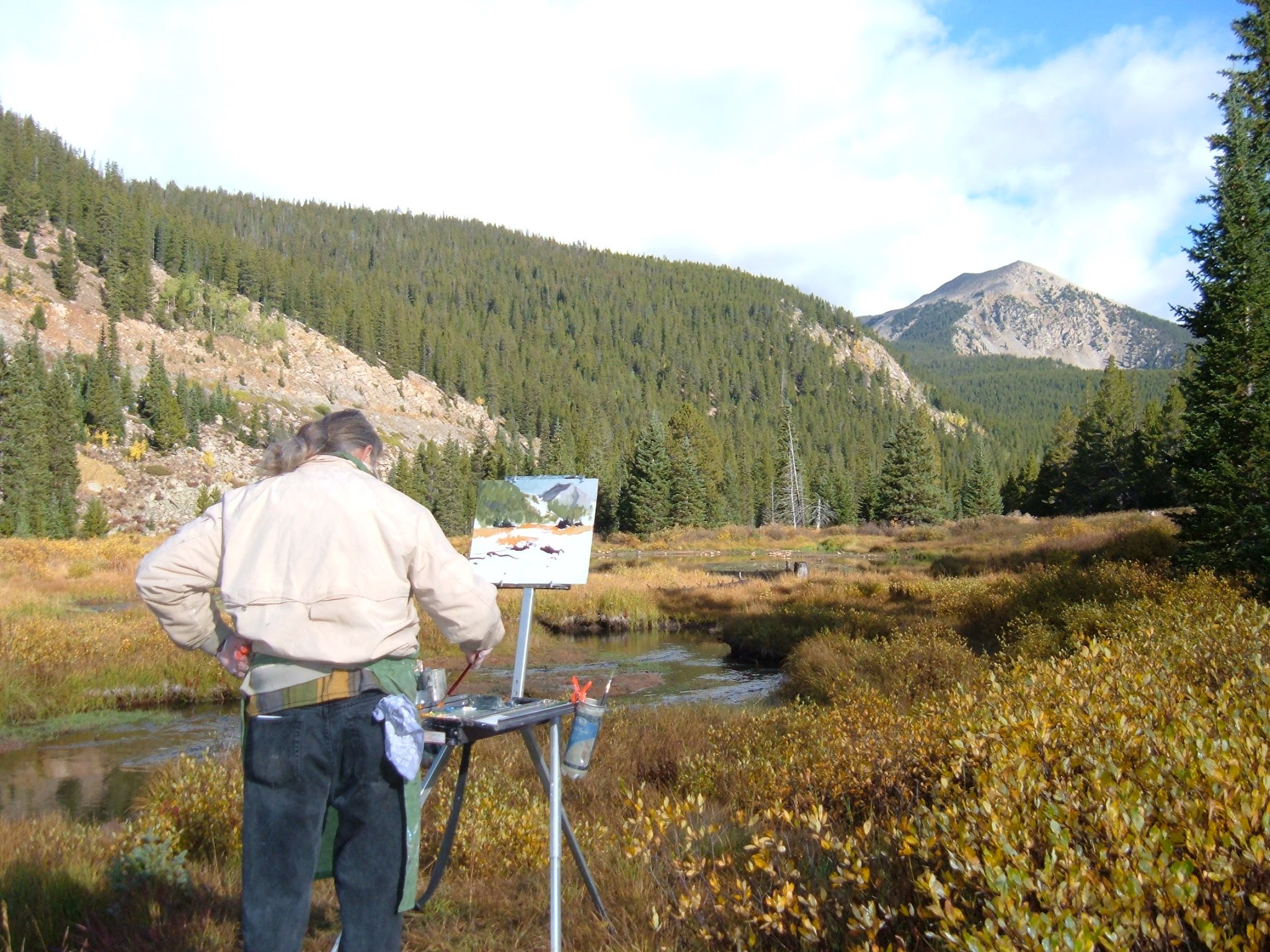Artist painting along a small pond with beautiful mountains all around.