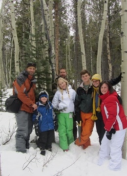 Family of seven cutting their Christmas tree in the forest and snow all around.