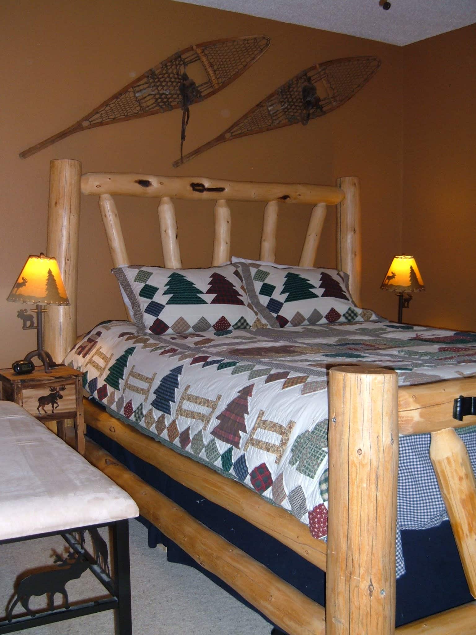 Bedroom with a beautiful queen size log bed, down comforter, tan walls, and a ceiling fan.