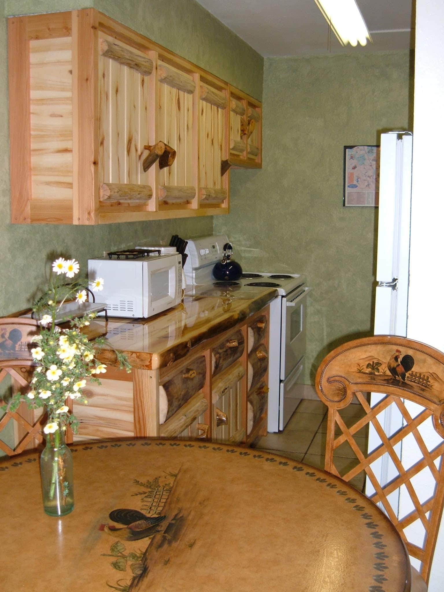 Kitchen with beautiful rustic log cabinets, tile floors, and faux green walls.  Dinning table with faux painting of a rooster.