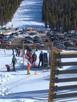 Parking lot at the base of a ski area with cars and people all around.