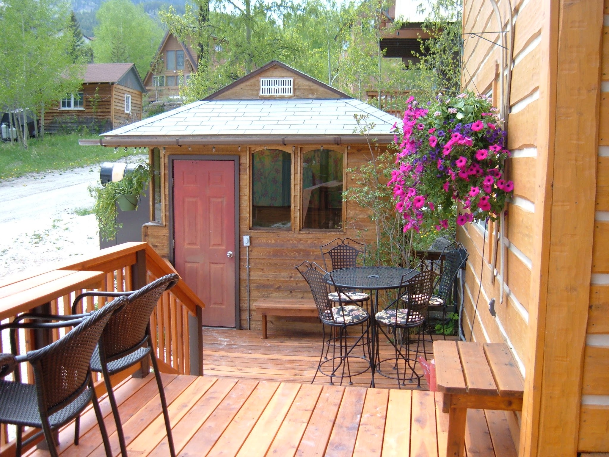 Wooded deck with large hanging pot of pink and purple flowers; both attached to the log sided condos with antique skis behind the the hanging flower pots.