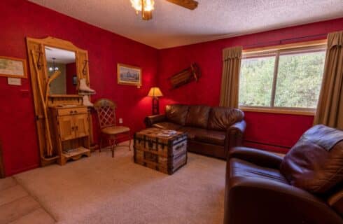 Living room with red walls, ceiling fan, antique trunk, leather brown sofa.