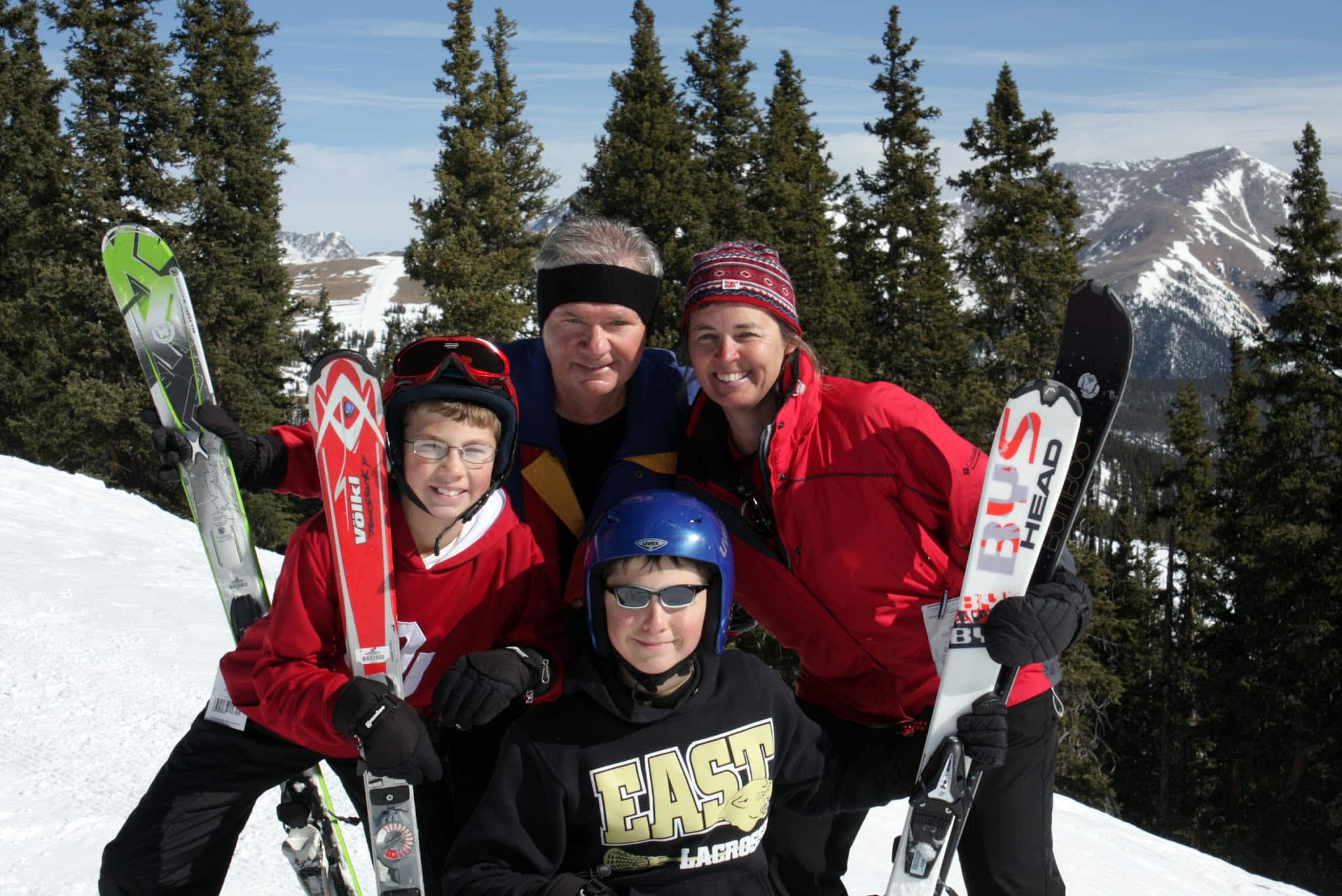 A family of four taking photos at a ski area with skis in hand.