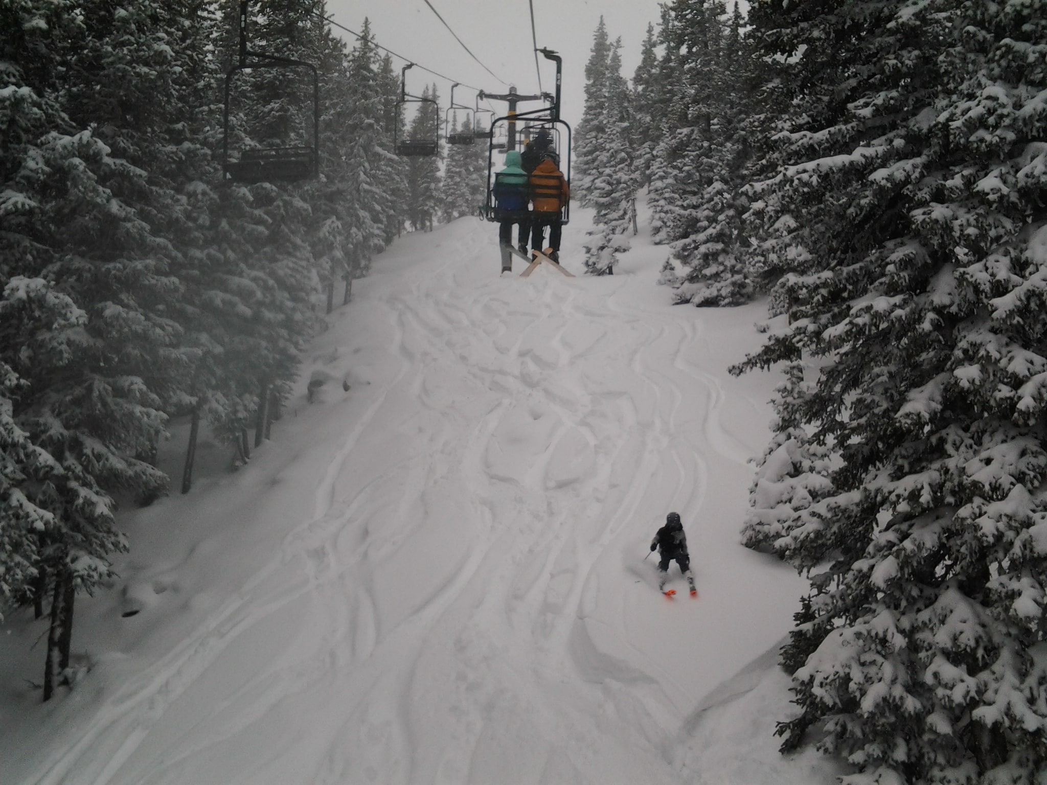 Winter snowy day with a skier skiing in powder on a steep hill below the chair lift.