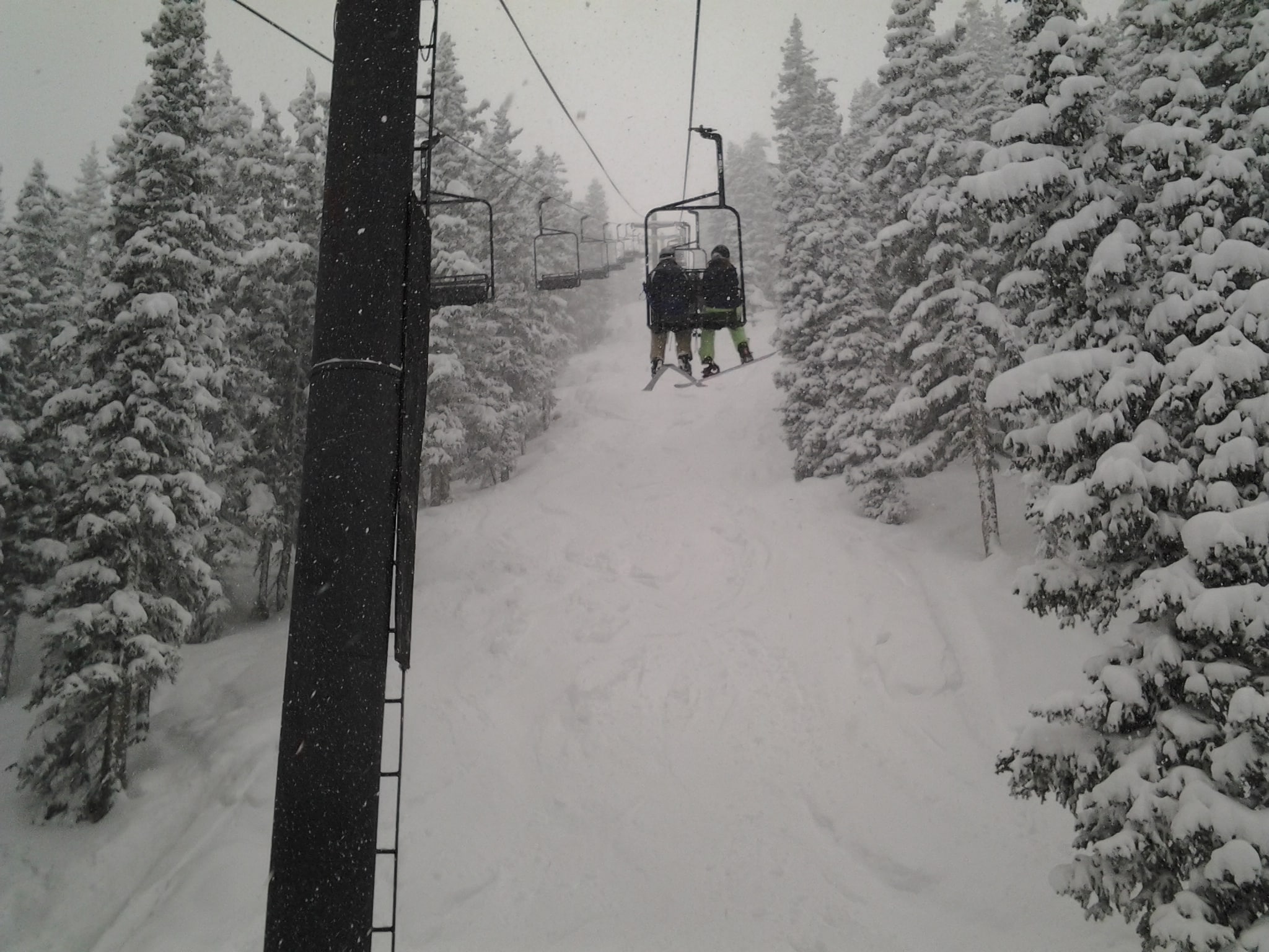 Snow winter day riding up a chairlift with snow covered trees on each side.