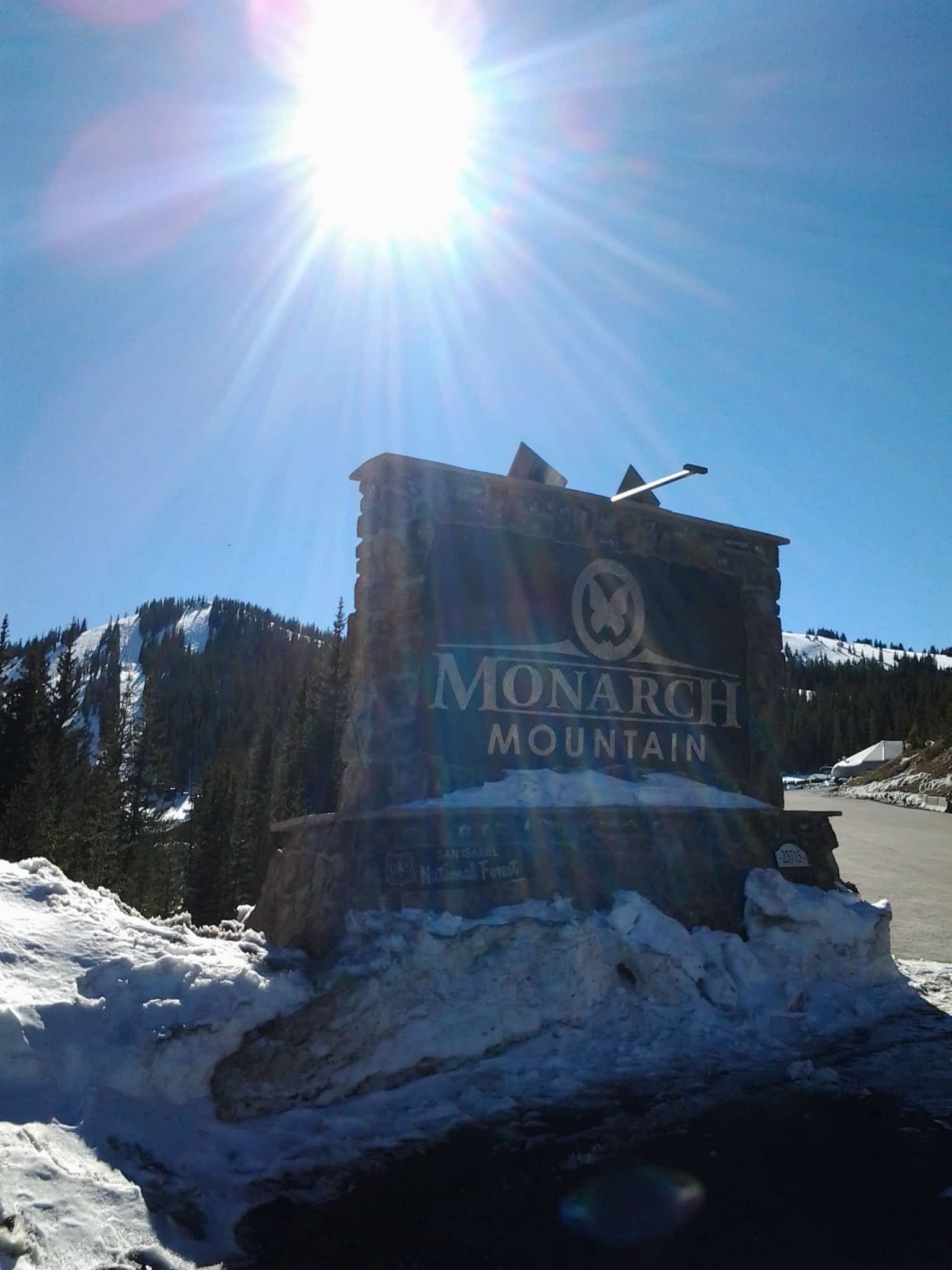 Sun shinning above the Monarch Mountain entrance sign, with the ski area in the distance all covered in snow