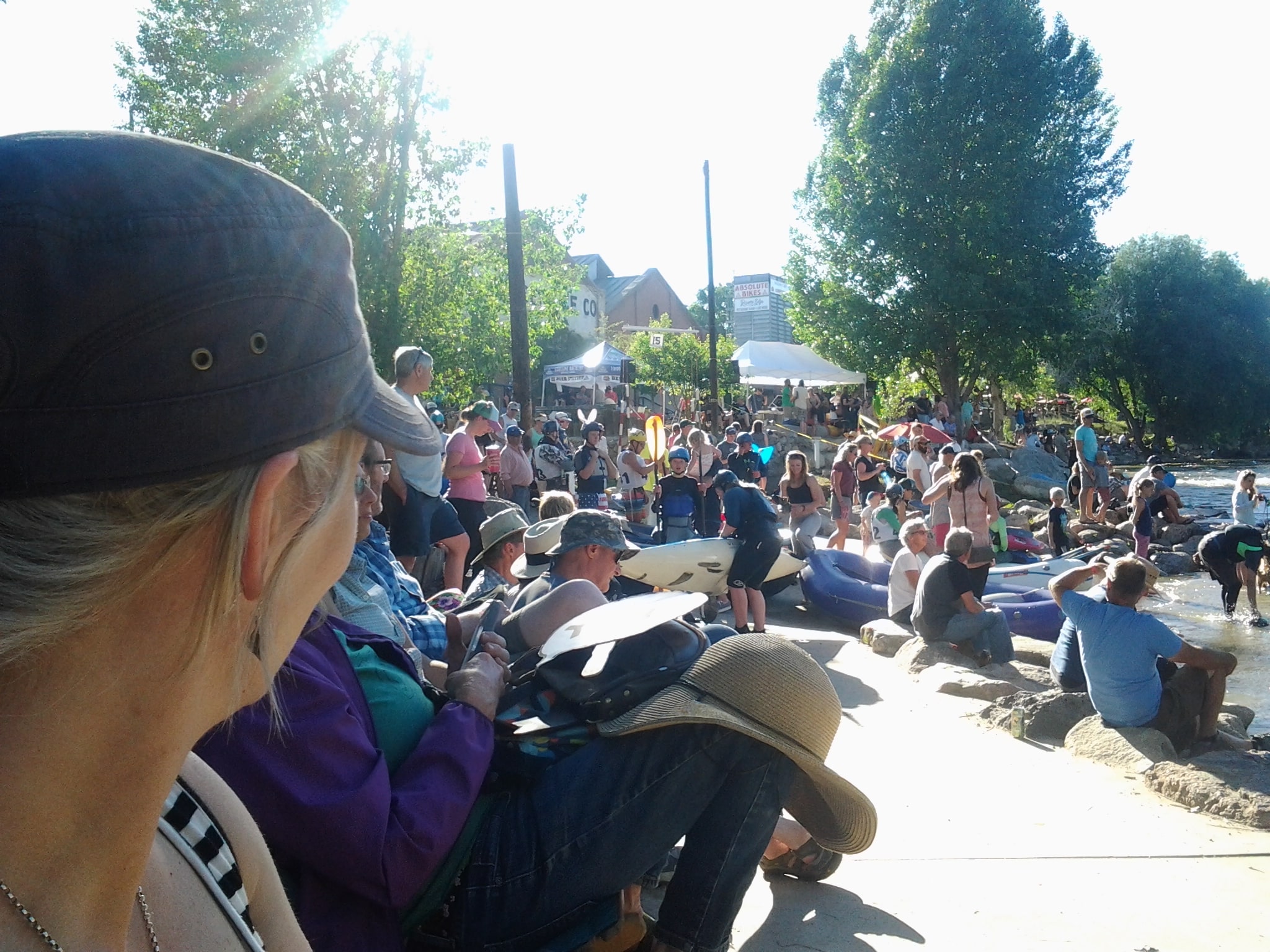 Lots of spectators sitting along the river bank watching the whitewater festival on a sunny day.