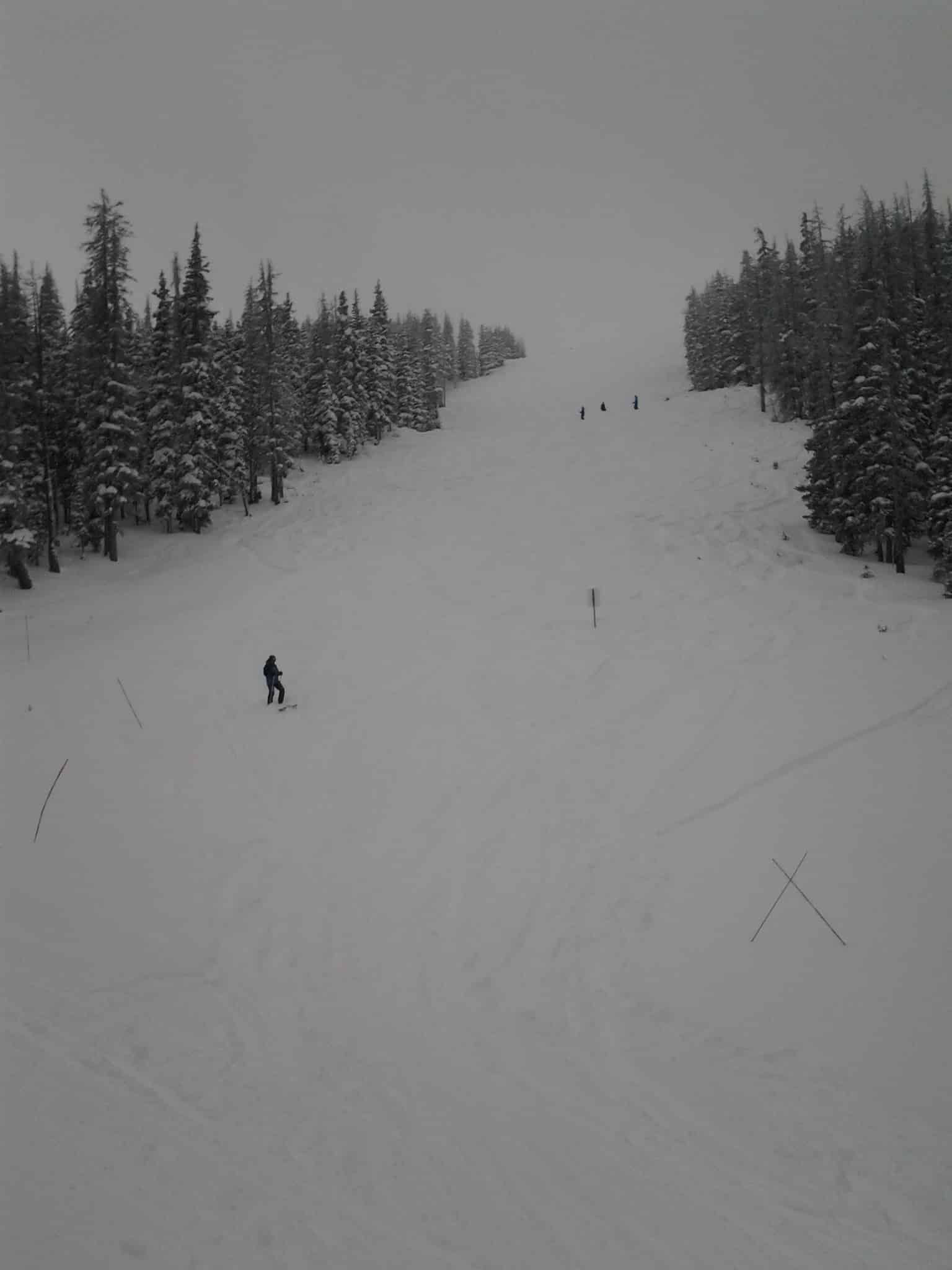 Ski slope with four skiing down a steep run on a snowy and cloudy day.
