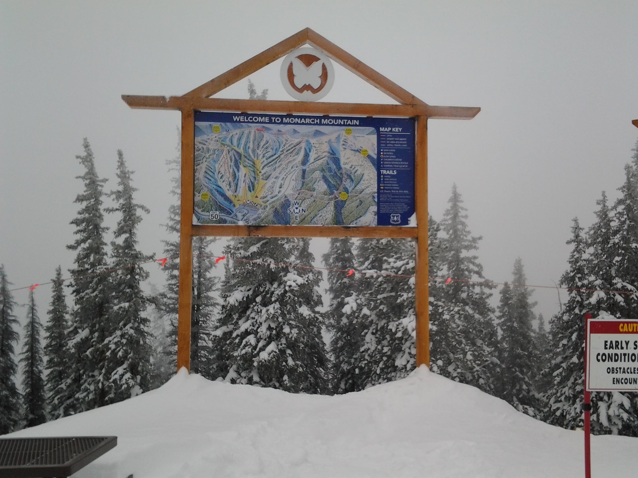 Large outdoor ski map at Monarch Mountain, on a cloudy and snowy day with pine trees covered in snow.