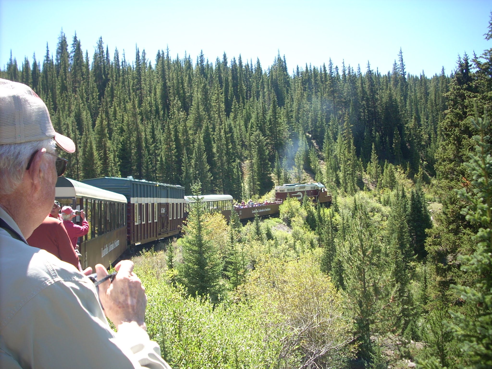 Outdoor photo of a train ride in the mountains on a sunny day with guests taking photos of the scenery.