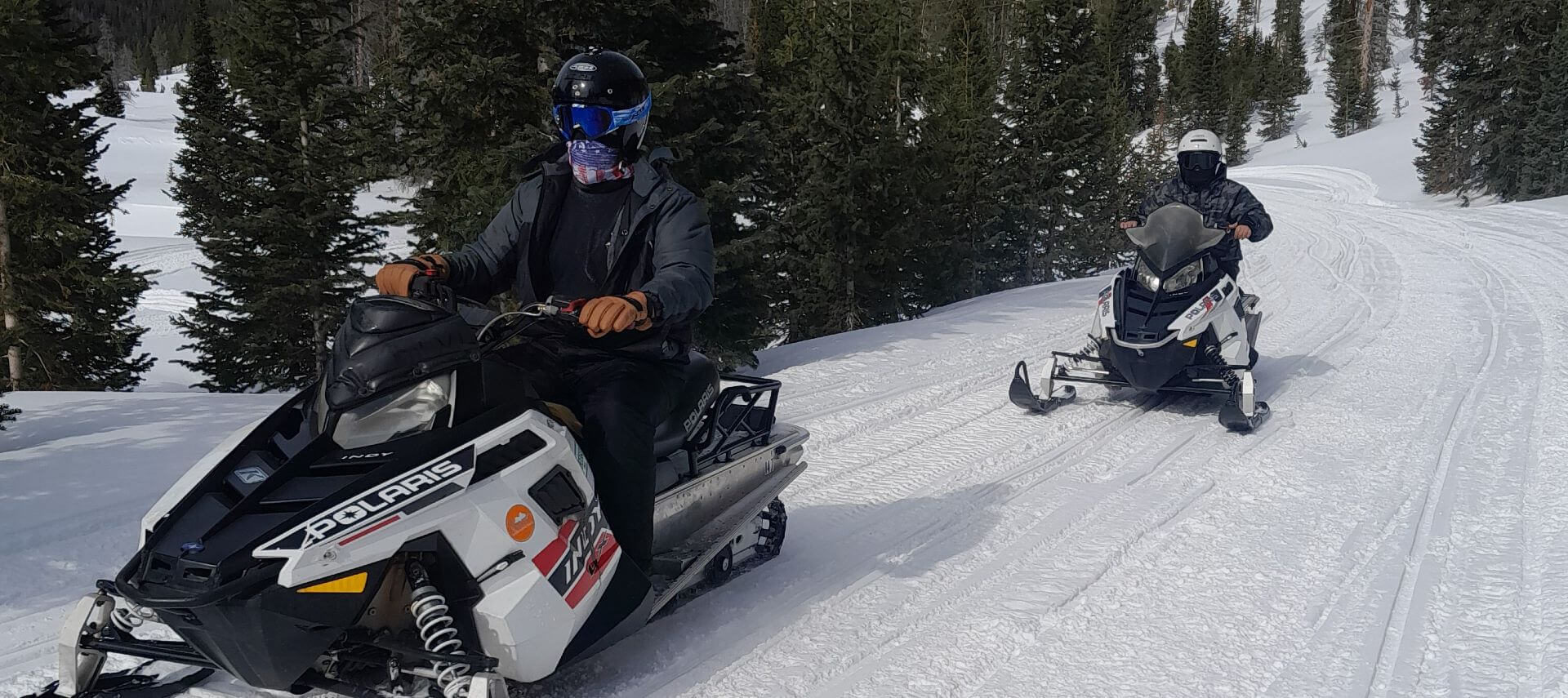 Exterior winter day with two snowmobile riders in the mountains.