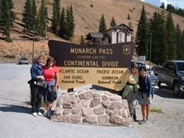 Four ladies with their hiking gear on, taking a photo at the Continental Divide sign on Monarch Pass.