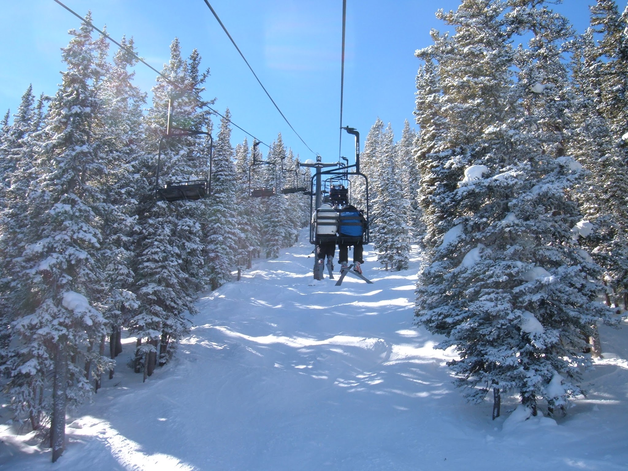 Chairlift ride through the narrow tree lined run. Blue ski with the sun shinning through the trees.