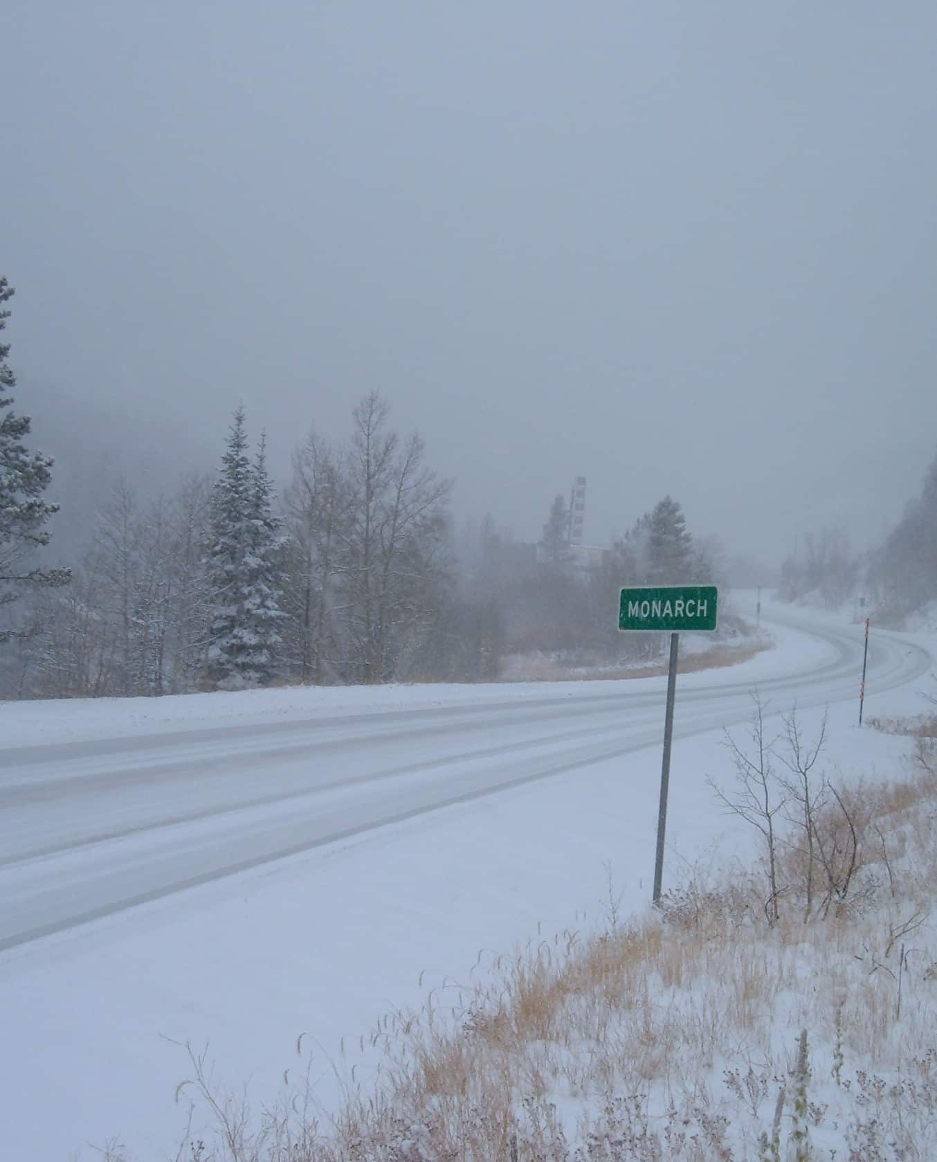 Monarch highway sign along a snowy mountain pass with fog all around.