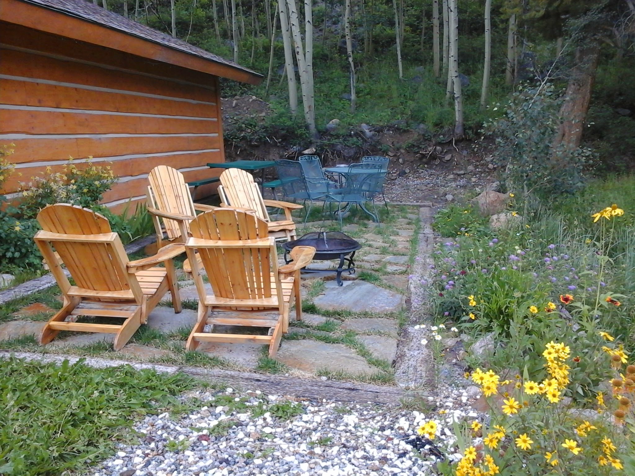 Stone patio with four chairs around a fire pit, tables, two wild flower rock gardens.