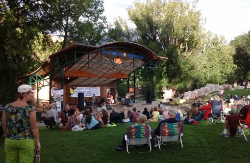 Outdoor pavilion surrounded by grass and large trees hosting a concert