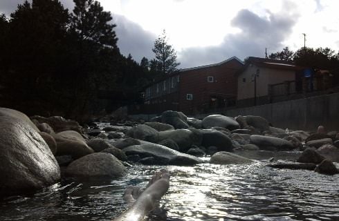 Hot springs surrounded by large rocks with a building, trees, and mountain in the background