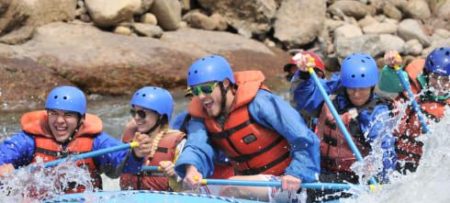 People wearing red lifejackets and blue helmets white water rafting