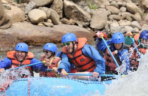 People wearing red lifejackets and blue helmets white water rafting