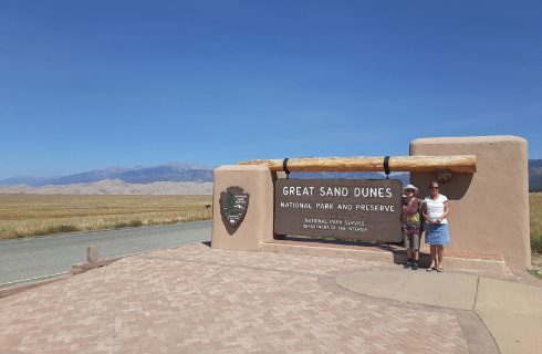 People standing by a large sign for Great Sand Dunes with the dunes and mountains in the background