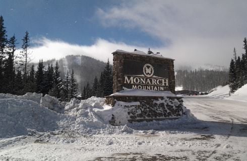 Large stone sign for Monarch Mountain covered and surrounded by snow with mountains in the background