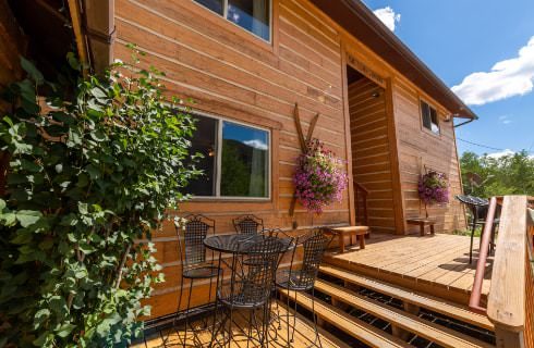 Exterior view of the property with wooden siding surrounded by green trees and shrubs and flowers