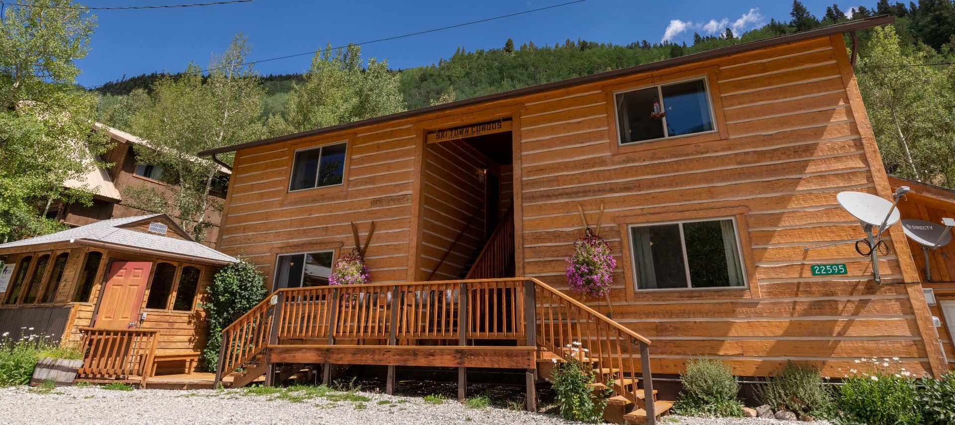 Exterior view of the property with wooden siding surrounded by green trees and shrubs and flowers