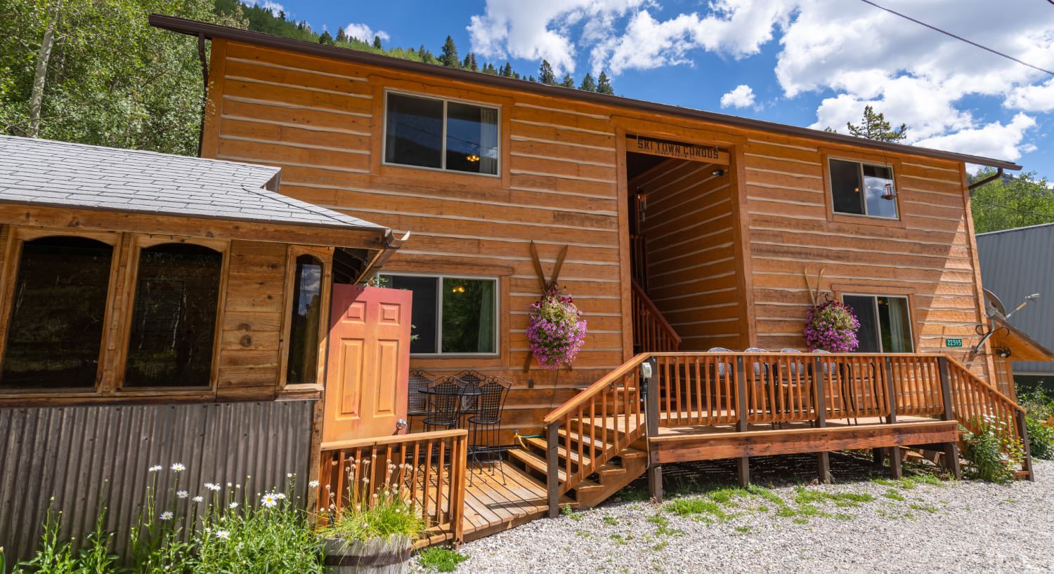 Exterior view of the property with wooden siding surrounded by green trees and shrubs and flowers