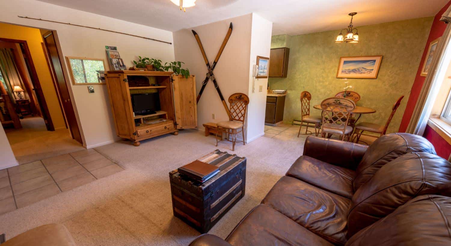 Large room with a living room with red and white walls, carpeting, brown leather sofa, kitchen with green walls, light colored tile flooring, and a dining area with wooden table and chairs