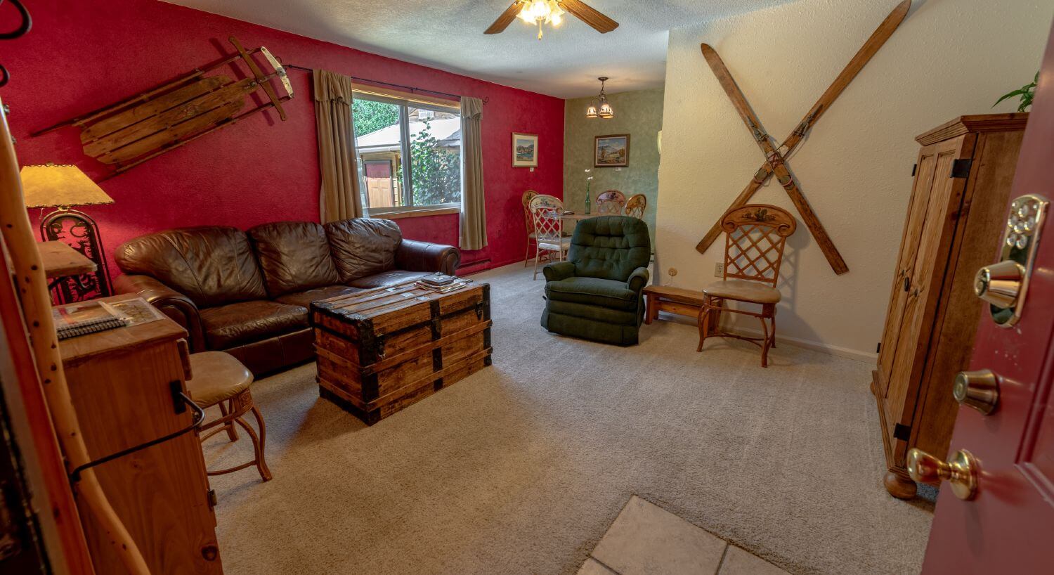 Living room with red walls, antique skis and sled attached to wall, chairs, leather sofa, light colored carpet.