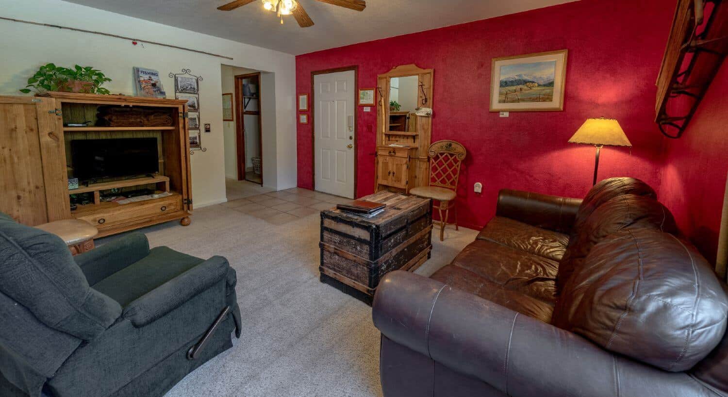 Living room with brown leather sofa, trunk, light carpet, with red white walls.