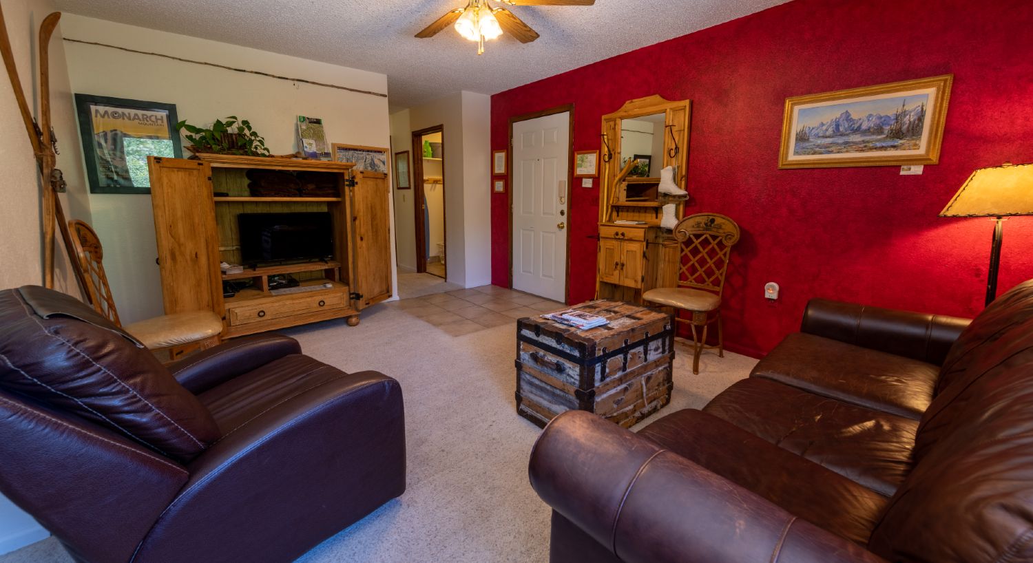 Living room with leather sofa, tv and blankets in a rustic armoire, with the hallway in the back.