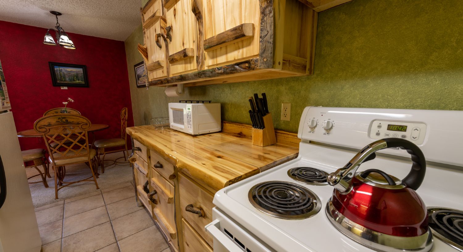 Kitchen with rustic log cabinets, tile floors, and a four burner stove and oven.
