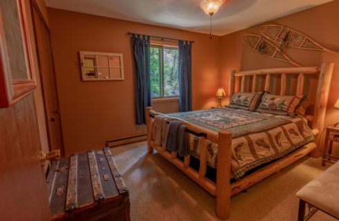 Bedroom with tan walls, carpeting, wooden log bed, homemade quilt, and wooden nightstand