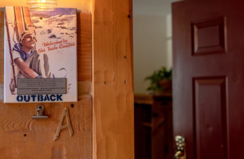 Close up view of a plaque hanging outside a room with a welcome message and the Outback room name