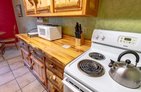 Kitchen with green and red walls, light colored floor tile, wooden cabinets, white stove, and white microwave