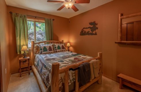 Bedroom with tan walls, carpeting, wooden log bed, homemade quilt, and wooden nightstand