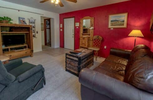 Outback condo Livingroom with antique trunk, leather brown sofa, painting on the read wall,, with a ceiling fan.