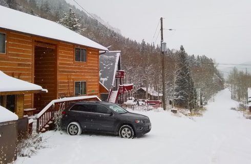 Exterior view of the property with wooden siding all covered in snow and surrounded by trees