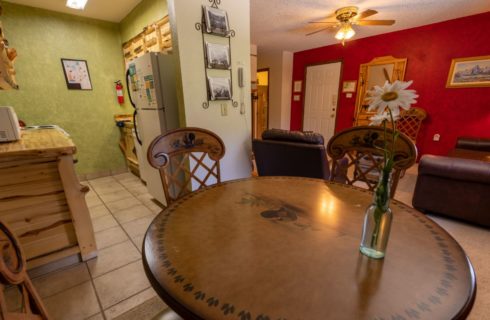 Large room with a living room with red and white walls, carpeting, brown leather sofa, kitchen with green walls, light colored tile flooring, and a dining area with wooden table and chairs